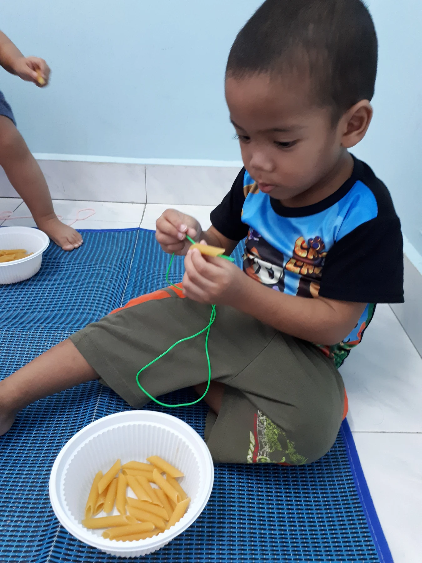Kanak-kanak menumpukan perhatian ketika memasukkan pasta pada tali hijau.